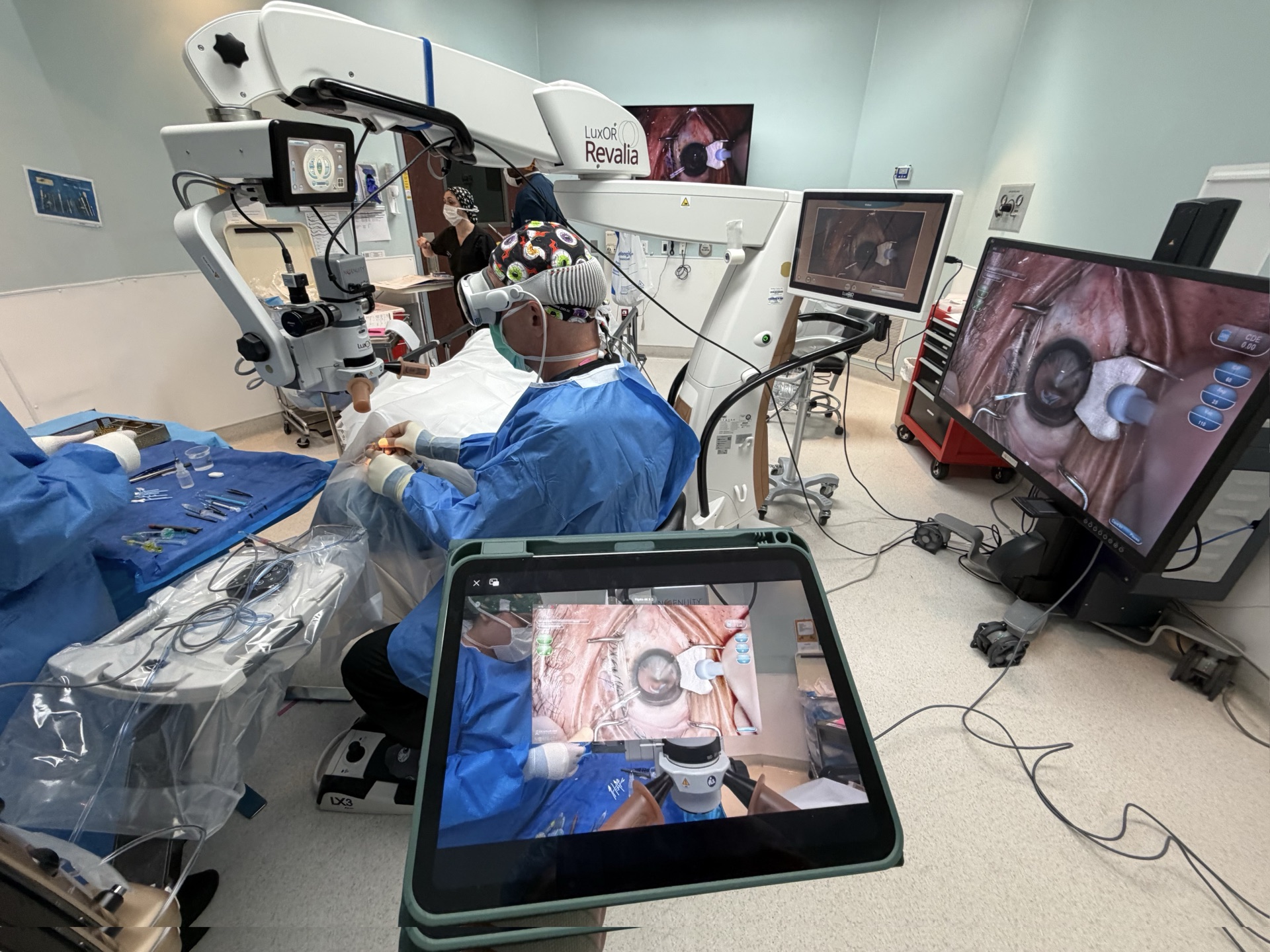 A surgeon wearing Apple Vision Pro at a digital microscope, with the live surgical view mirrored on an iPad and operating-room monitors.